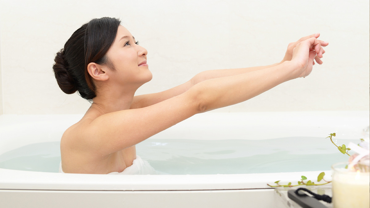 浴槽でお風呂に浸かりながら伸びをする女性